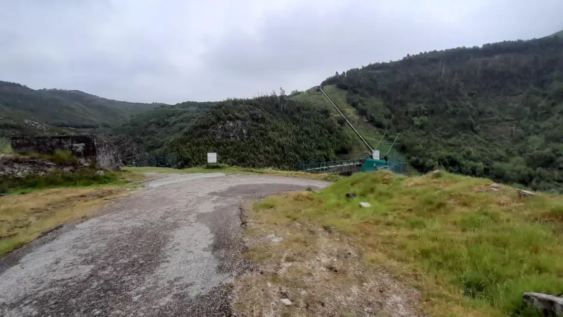 Camino de acceso a la fervenza da roca, con tuberías y vegetación en la ladera.