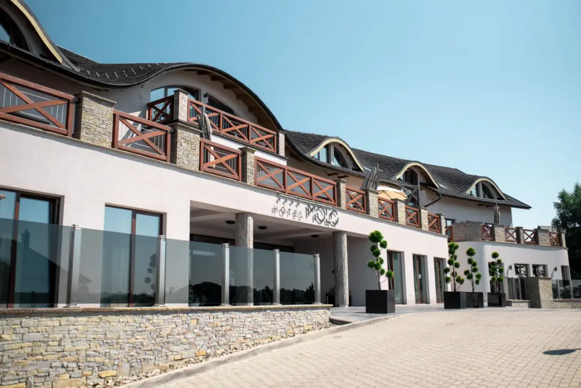Elegancki hotel Molo Resort z drewnianymi balustradami i kamienną podmurówką. Sprawdź molo resort ceny i zarezerwuj pobyt.