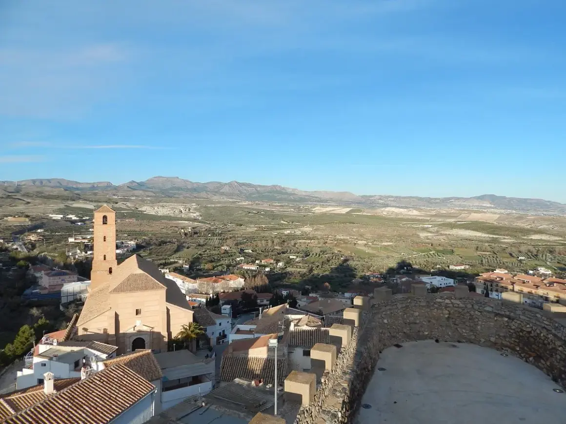 Vistas de Serón que ver: iglesia con campanario, tejados y paisaje rural montañoso bajo un cielo azul.