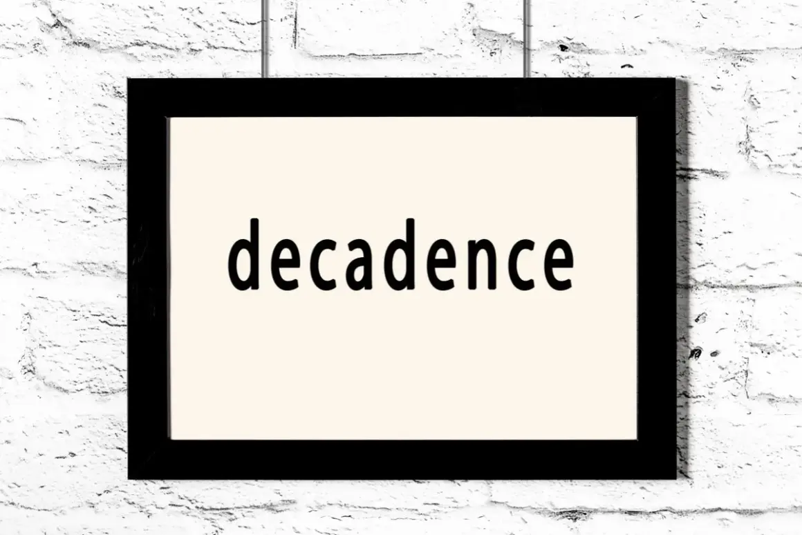Czarno-biały obraz z napisem "decadence" na jasnym tle, wiszący na białej ceglanej ścianie. To pytanie: co to dekadentyzm?
