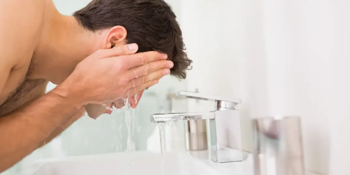 Mann wäscht sein Gesicht mit kaltem Wasser. Er hält seine Hände unter den Wasserhahn, um das Gesicht zu erfrischen.