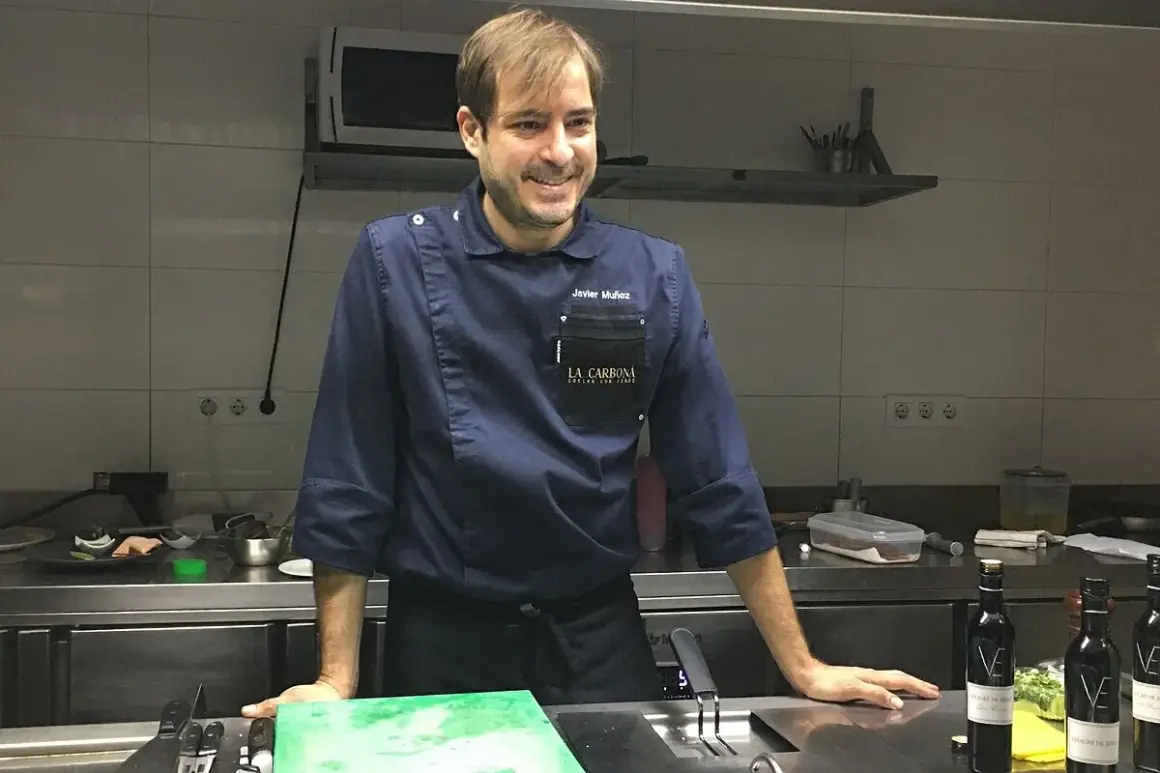 Javier Muñoz chef sonríe en la cocina, con su uniforme azul y el logo de "La Carbona".