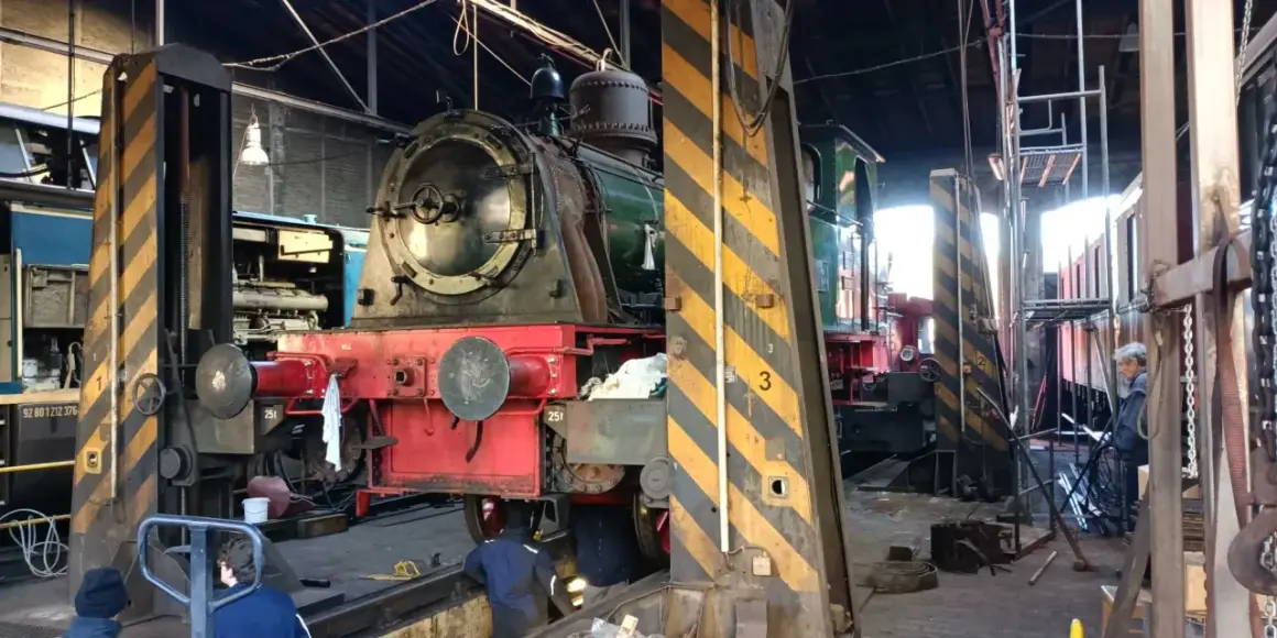 Im Eisenbahnmuseum Dieringhausen stehen mehrere Dampflokomotiven zur Wartung bereit. Eine rote und grüne Lokomotive ist im Vordergrund zu sehen.