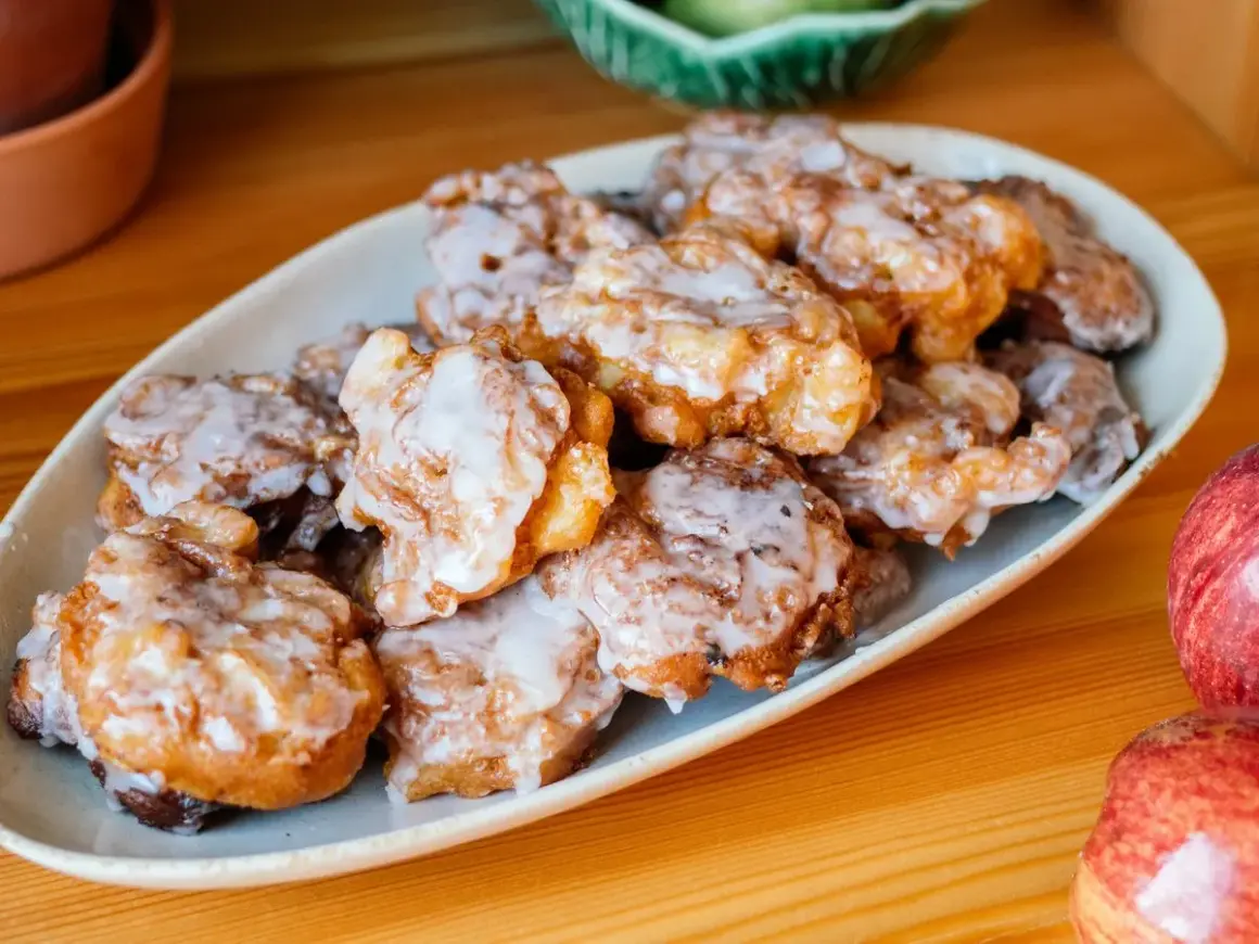 Leckere Apfelkrapfen in der Pfanne, goldbraun gebacken und mit Zuckerguss überzogen, liegen auf einem Teller.
