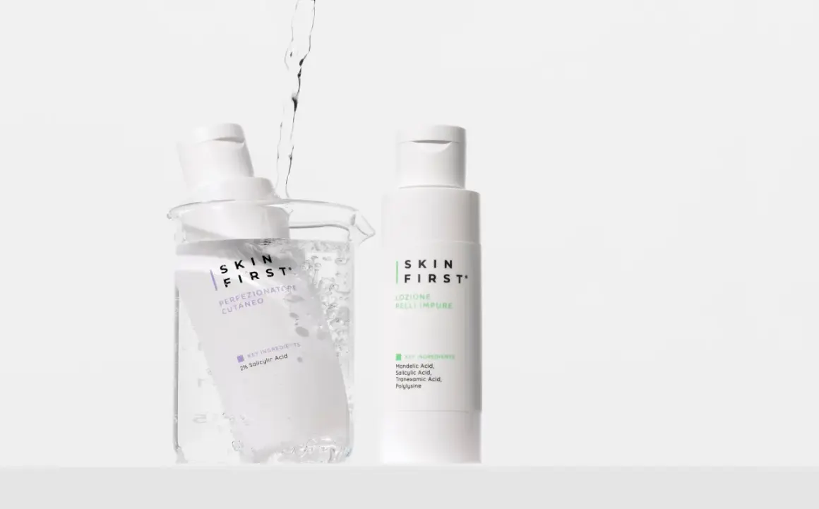 Due flaconi di tonico viso Skin First, uno immerso in un becher con acqua e bollicine, l'altro in piedi.