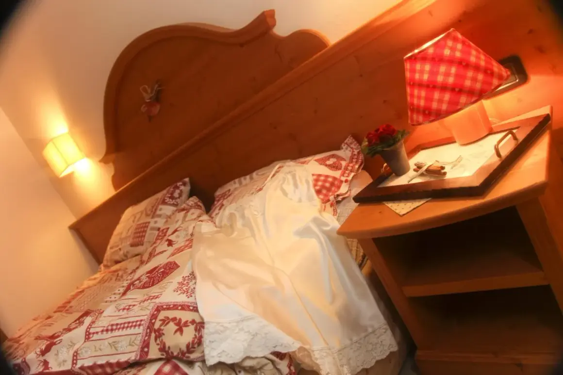 Camera accogliente all'hotel La Romantica Moena, con letto decorato e comodino con fiori.