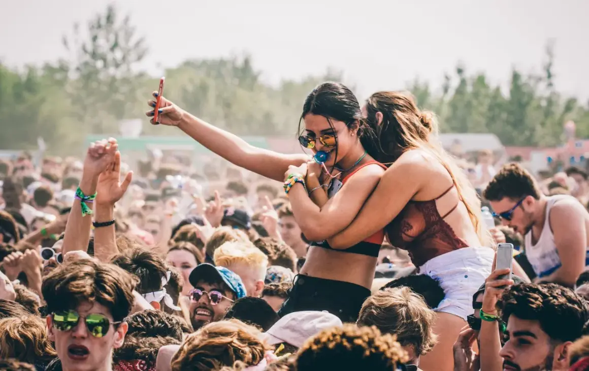 Menschen feiern ausgelassen beim **pulse open air**. Eine Frau hält ihr Handy hoch, während eine Freundin sie umarmt.
