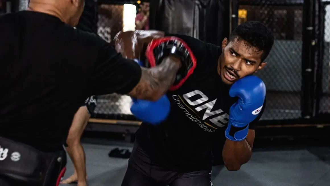 Fighter in blue gloves dodges an overhand punch during intense MMA training.