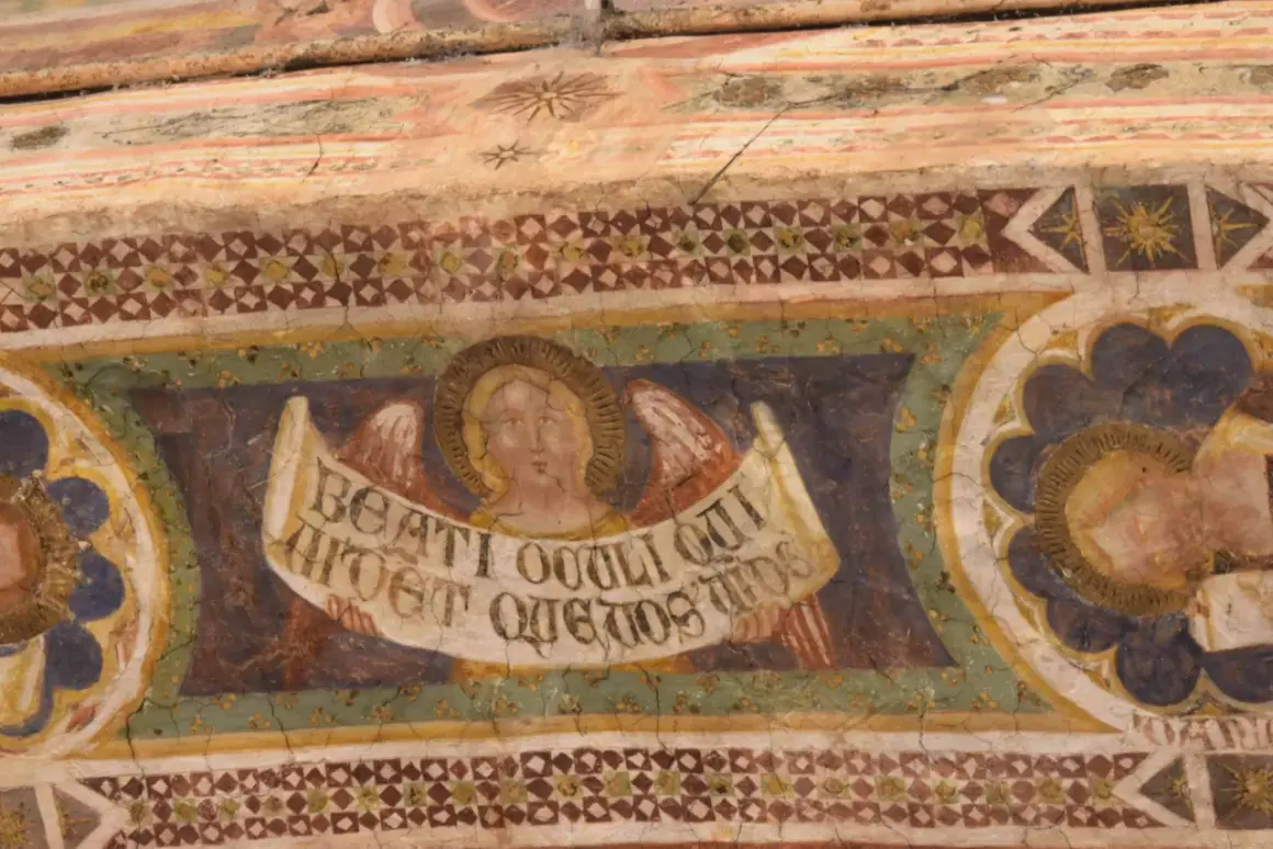 Angeli con pergamena negli affreschi dell'abbazia di Pomposa. Dettaglio di un volto angelico con ali e iscrizione latina, parte di un ciclo pittorico antico.