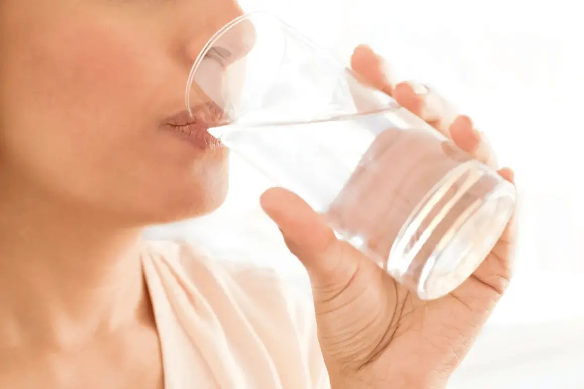 Une personne boit un verre d'eau, un geste simple pour savoir comment bien s'hydrater et rester en forme.