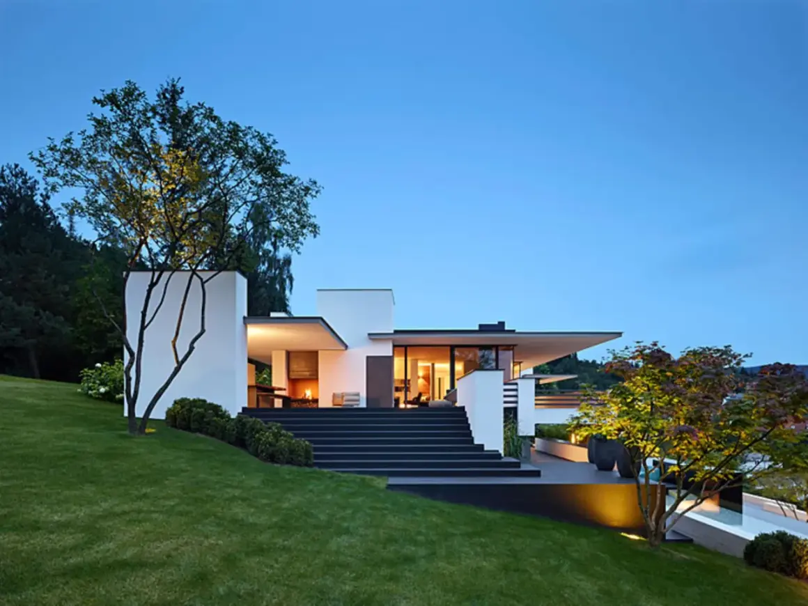 Moderne Villa mit breiter, dunkler Treppe zum Hauseingang. Tolle Ideen für Haus und Treppe, beleuchtet bei Dämmerung.