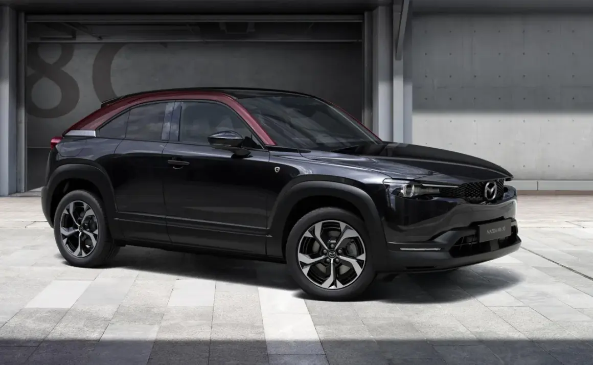 Czarna Mazda MX-30 z czerwonym dachem, prezentująca swoje kompaktowe mazda mx 30 wymiary, stoi przed betonową ścianą z numerem 80.