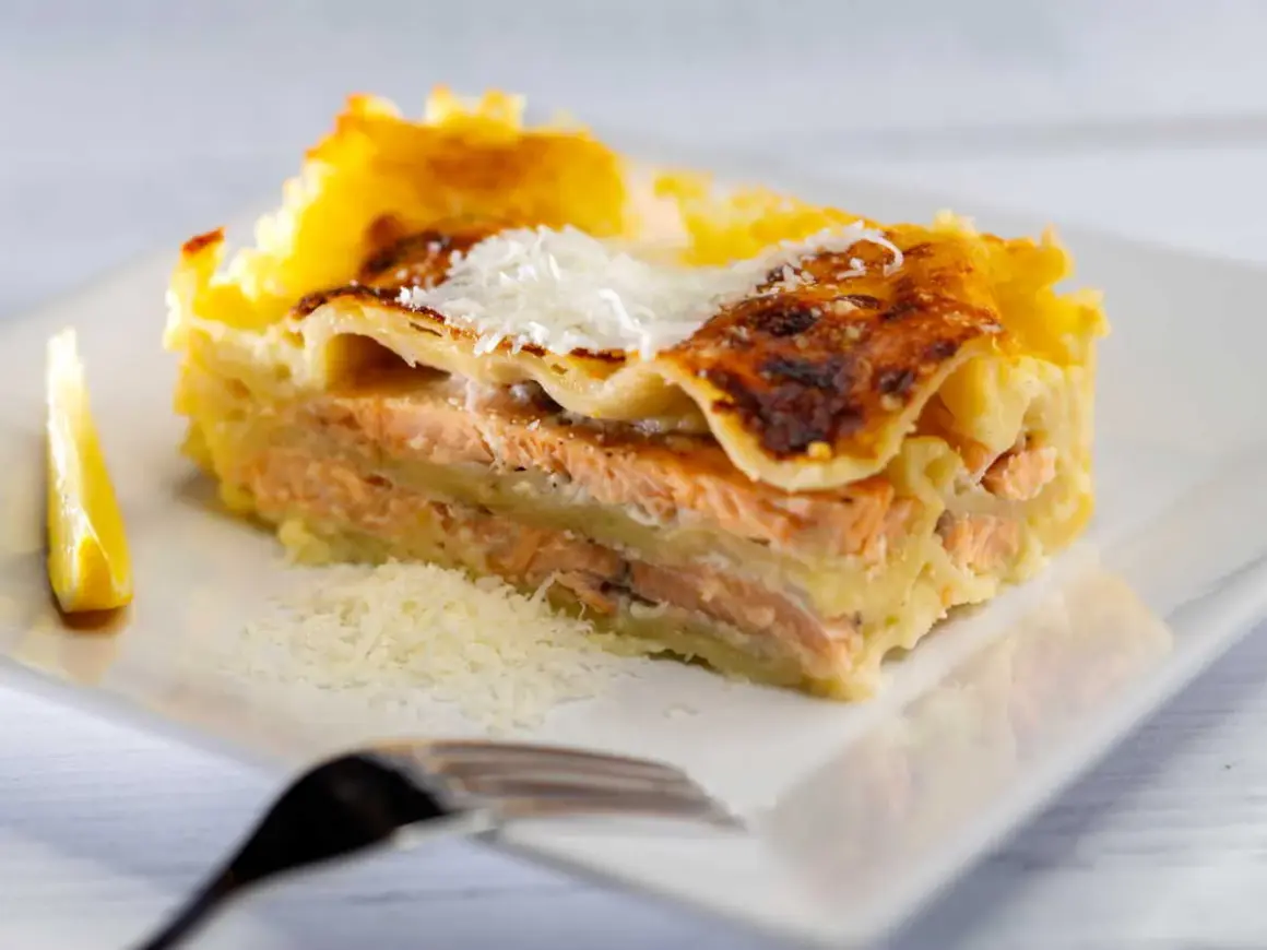Une part généreuse de lasagne saumon, dorée au four, garnie de parmesan râpé et accompagnée d'un quartier de citron.