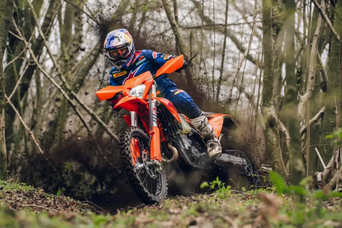 Piloto en una KTM 490 Adventure derrapando en un sendero boscoso, levantando barro.