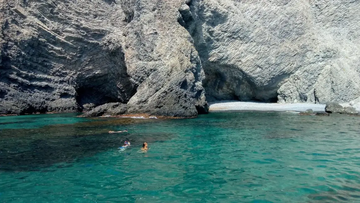 Gente nadando y haciendo snorkel en las aguas cristalinas de la cala puente Almería, rodeada de imponentes acantilados rocosos.