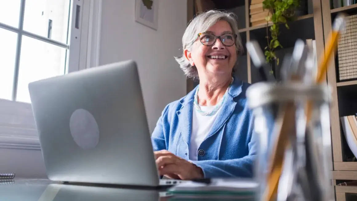 Lächelnde Frau am Laptop, die überlegt, wie sie Rente beziehen und vollzeit arbeiten kann, ohne die Steuerklasse zu ändern.