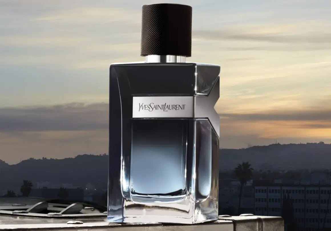 Elegancka butelka Y Yves Saint Laurent Y 100ml na tle zachodzącego słońca nad miastem.