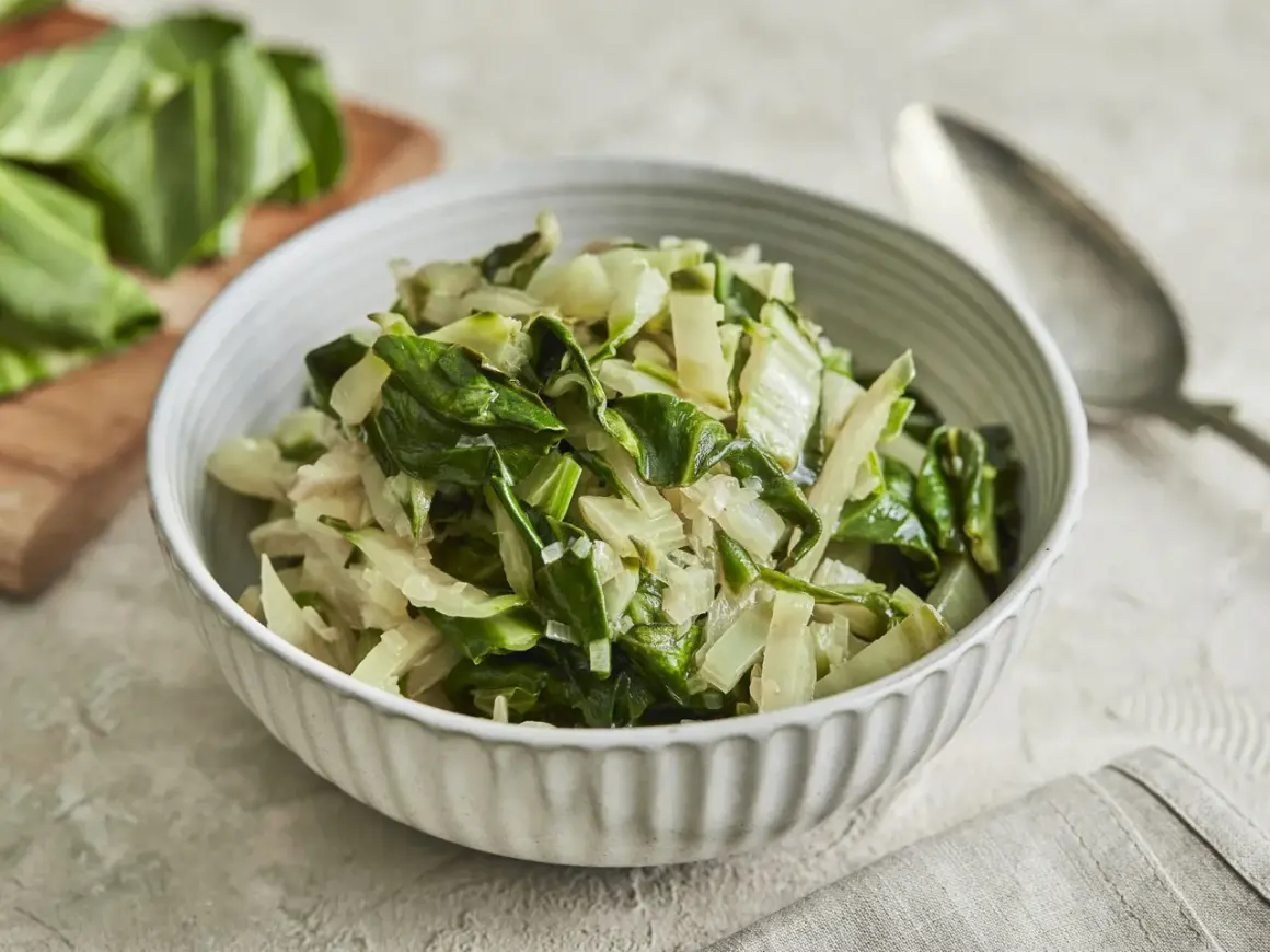 Schüssel mit gedünstetem Mangold, perfekt für ein einfaches Mangold Rezept. Frische Blätter liegen daneben.