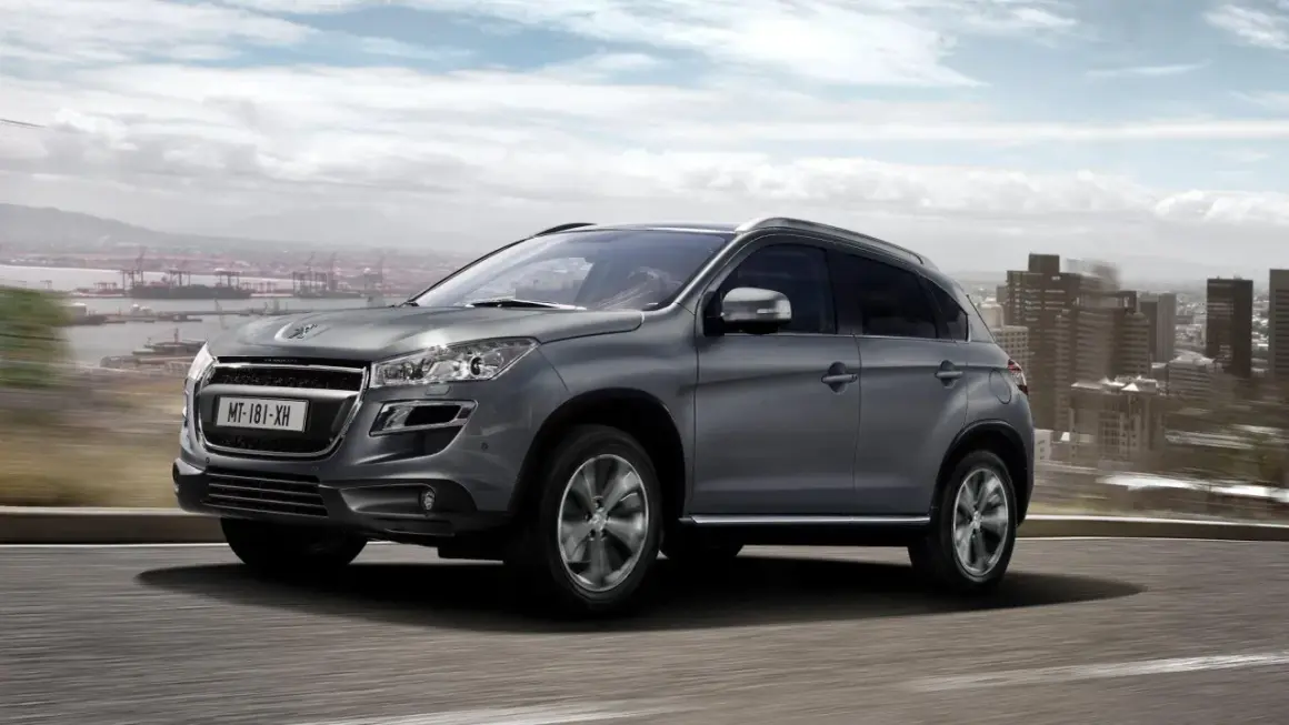 Szary Peugeot 4008 jedzie po drodze z widokiem na miasto i port.