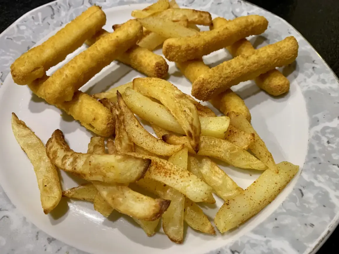 Ein Teller mit knusprigen belgischen Pommes, einige dick geschnitten, andere als Stäbchen frittiert.