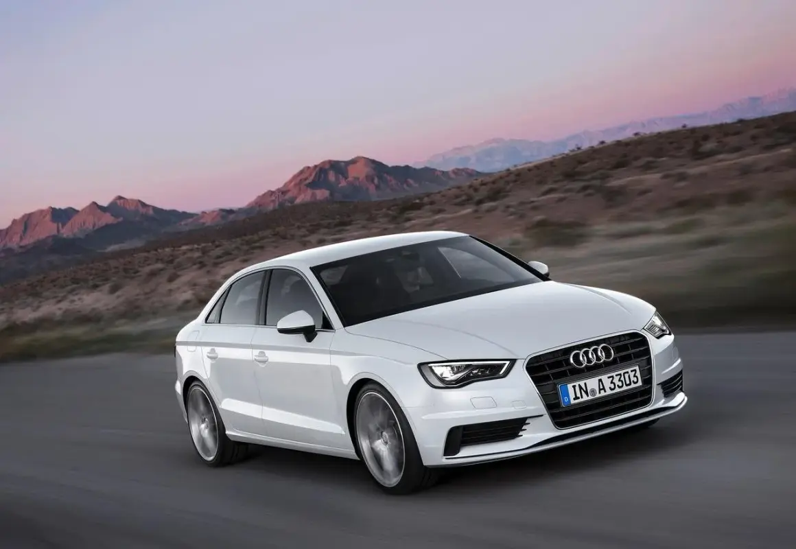 Białe Audi A3 jedzie po drodze w górach. Jego lekka konstrukcja i dynamiczny wygląd podkreślają jego sportowy charakter.