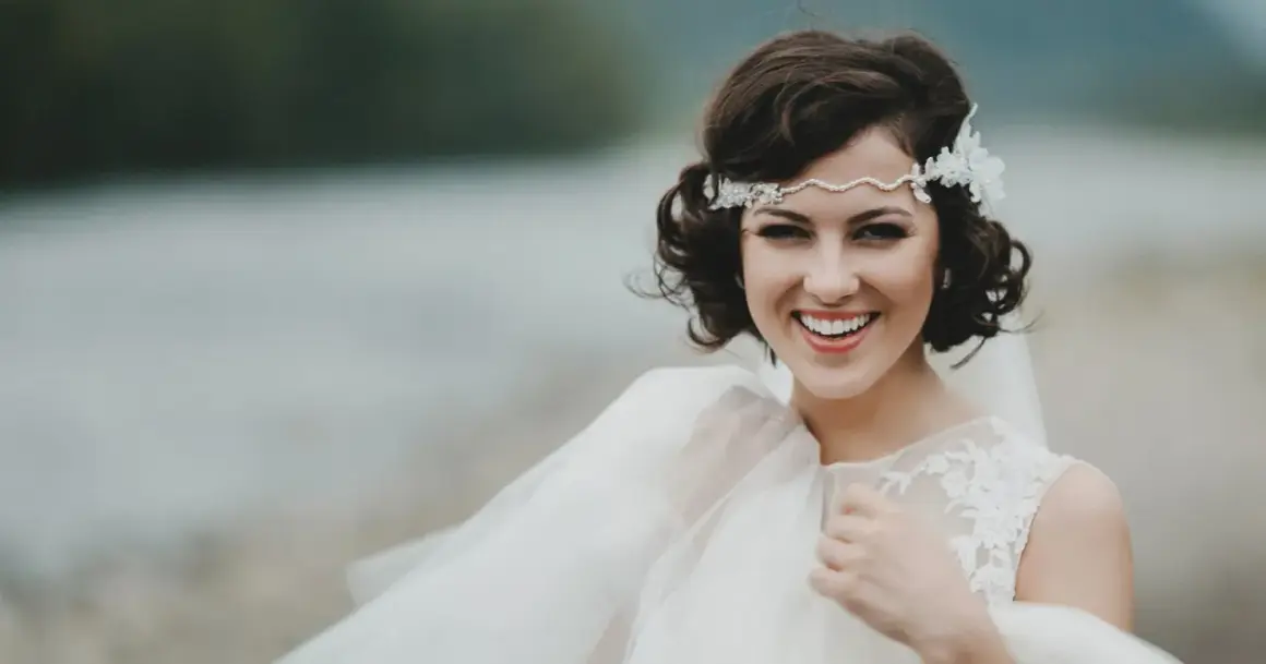 Novia sonriente con semirecogido pelo corto boda, diadema de perlas y encaje, velo vaporoso.