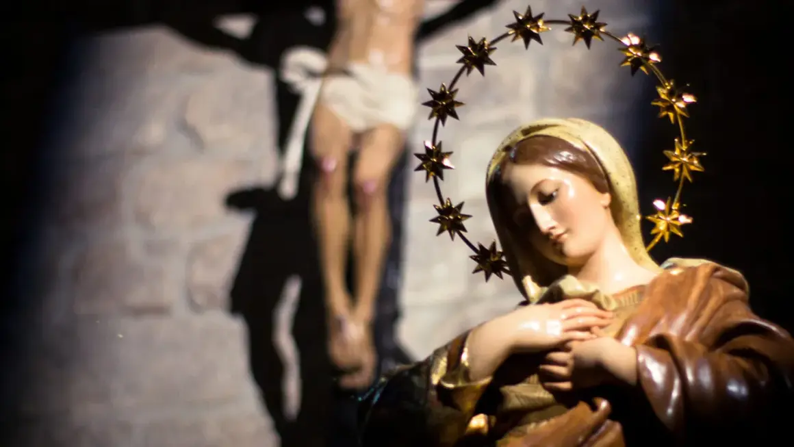 Figurka Matki Bożej z gwiazdami na głowie, w tle ukrzyżowany Jezus. Symbol bólu i cierpienia, jak w różańcu części bolesne.