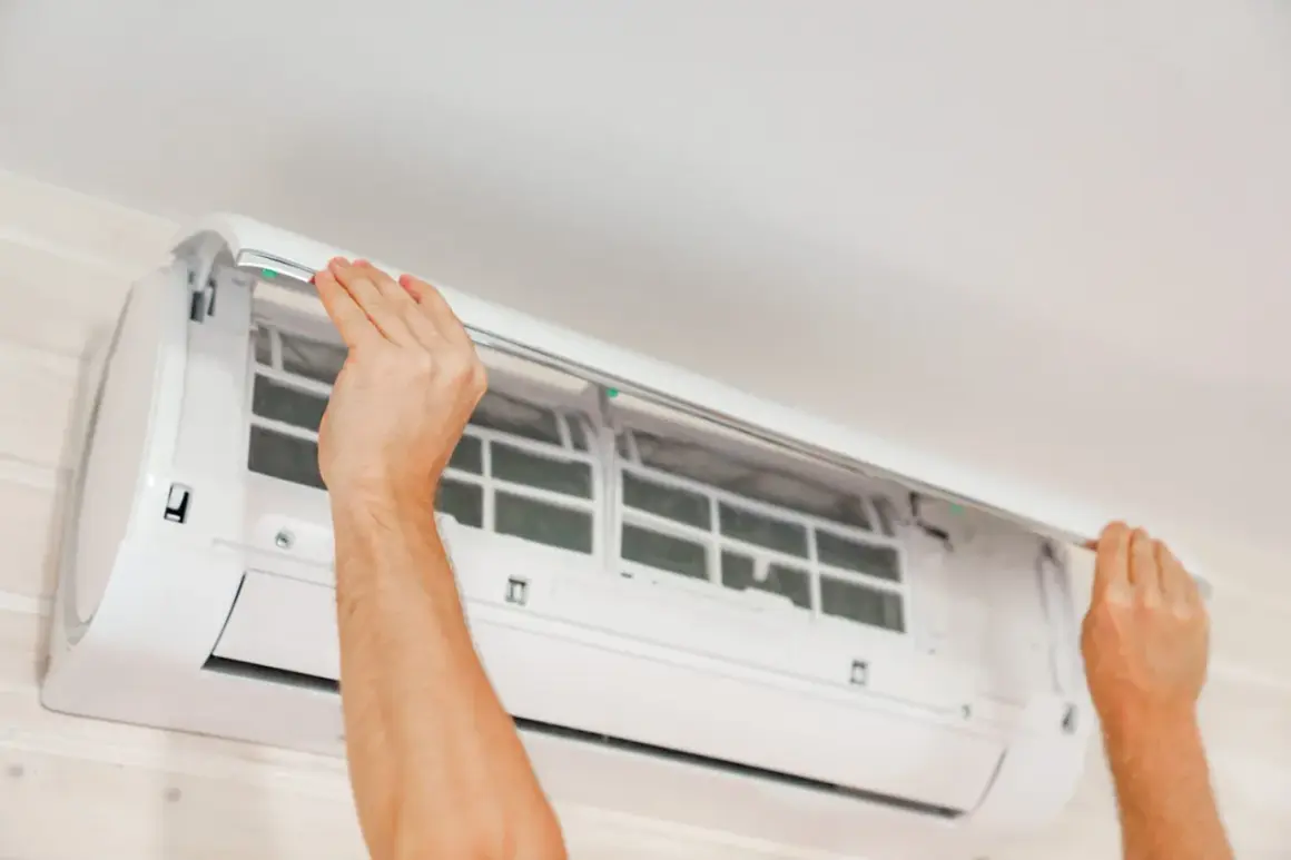 Mains ouvertes pour le nettoyage clim. Les filtres sont visibles à l'intérieur de l'unité murale.