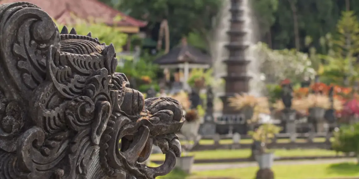 Eine detaillierte Steinskulptur eines Fabelwesens im Vordergrund, im Hintergrund ein Garten mit Brunnen und Pflanzen.