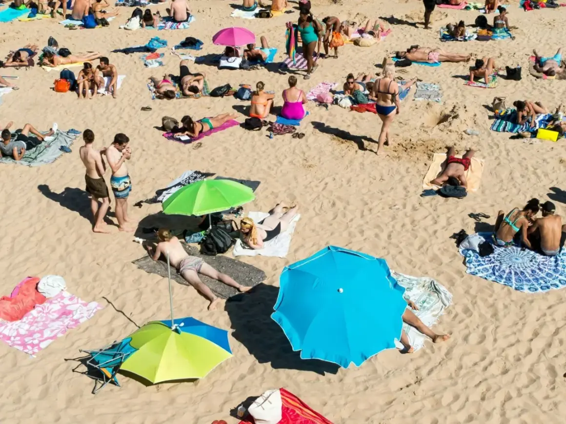 Wakacje pod gruszą na plaży. Ludzie opalają się, odpoczywają pod parasolami, ciesząc się słońcem i piaskiem.