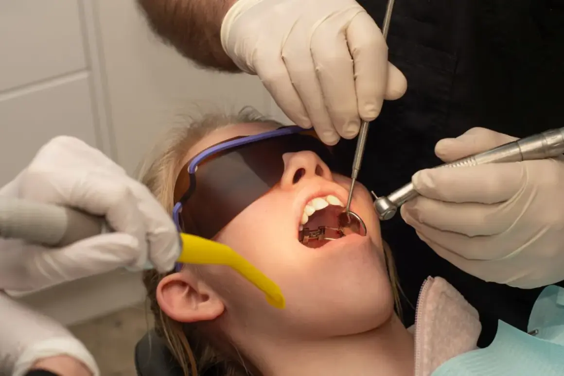 Usta pacjentki otwarte, w nich aparat ortodontyczny. Dentysta używa wiertła i lusterka. Wygląda jakby przygotowywał się do zabiegu, a nie jakby oglądał zwierzęta z rodziny **hyrax**.