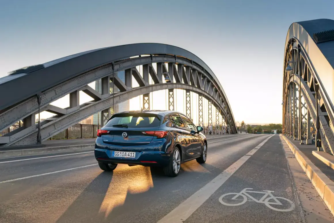 Ciemnoniebieska Astra jedzie po moście pod zachodzącym słońcem. Dostępne akcje serwisowe Opel dla Twojej Astry.