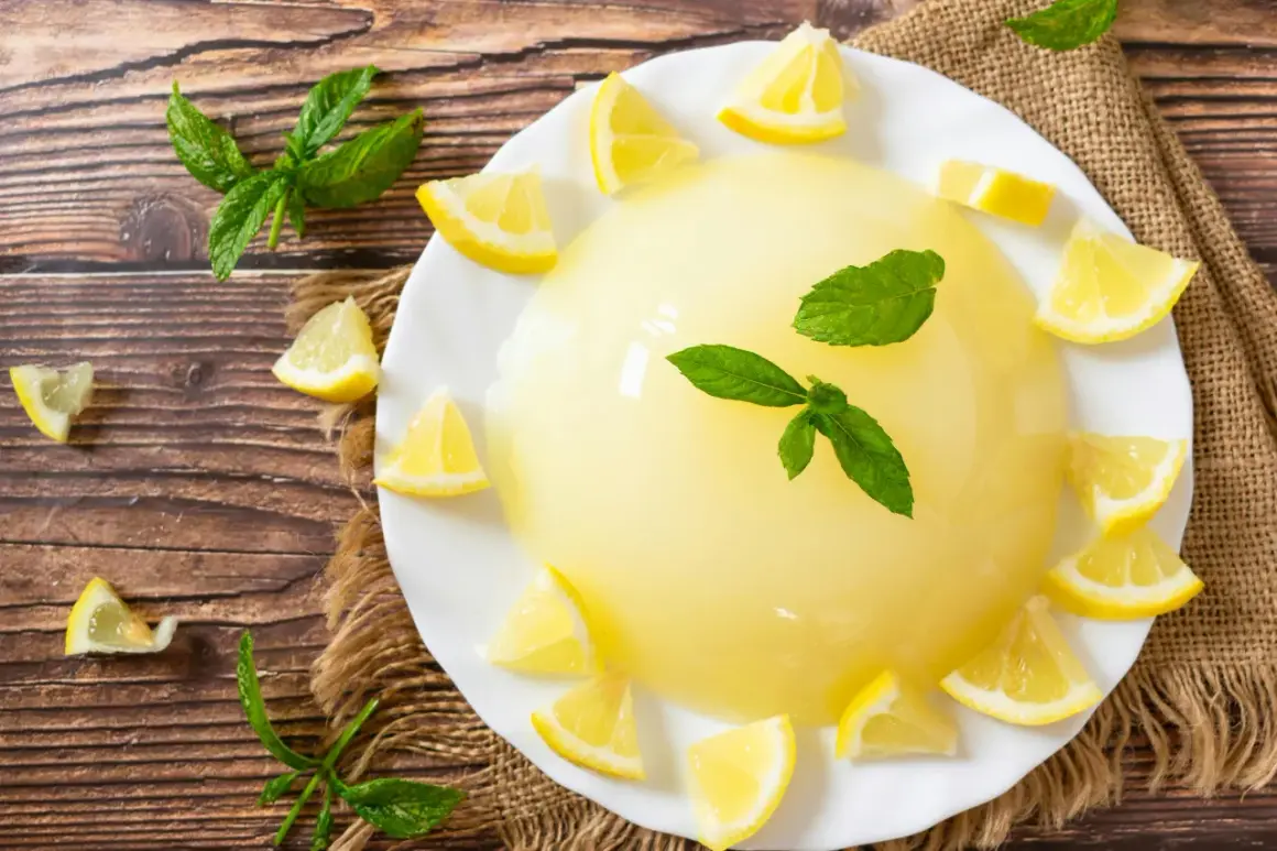 Un rinfrescante gelo di limone, guarnito con spicchi di limone e foglie di menta, su un piatto bianco, circondato da limoni e menta su un tavolo di legno.