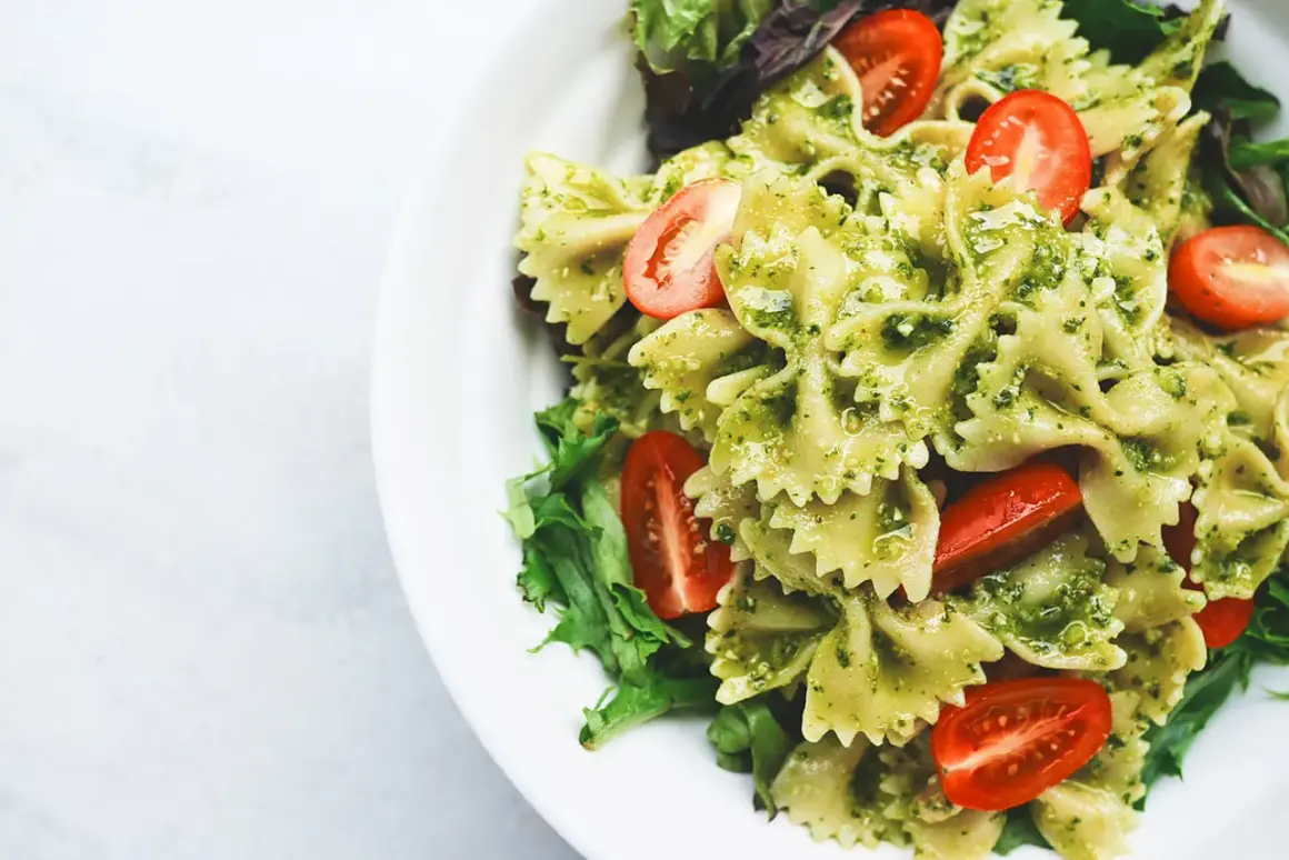 Un piatto invitante di pasta fredda al pesto, con farfalle condite e pomodorini freschi, guarnito con insalata verde.