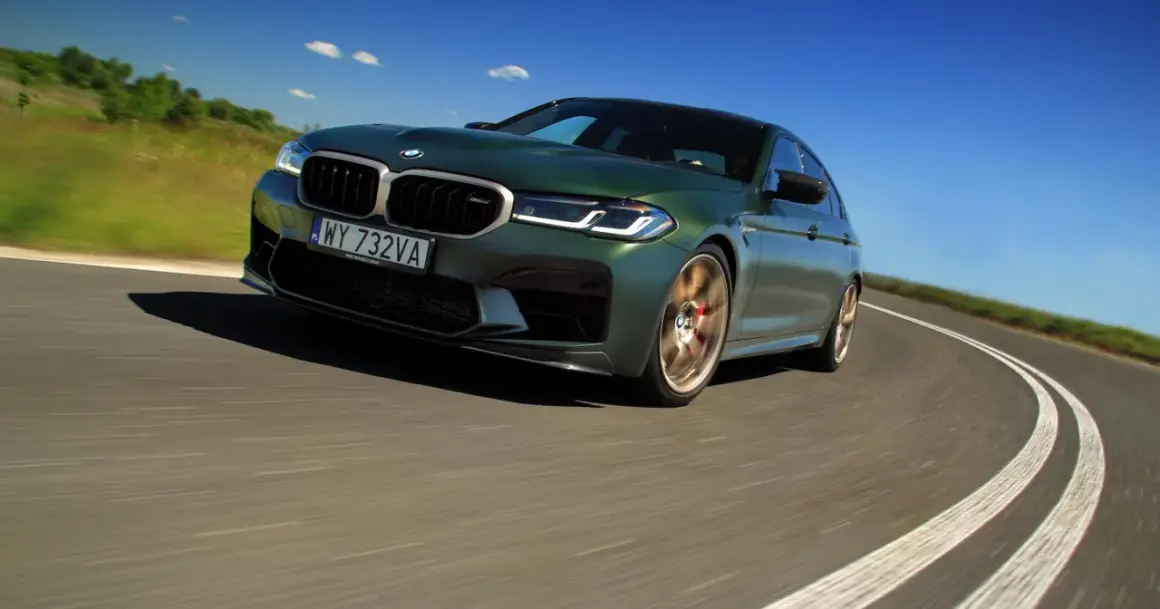 Zielony BMW M5 CS na zakręcie drogi pod błękitnym niebem.
