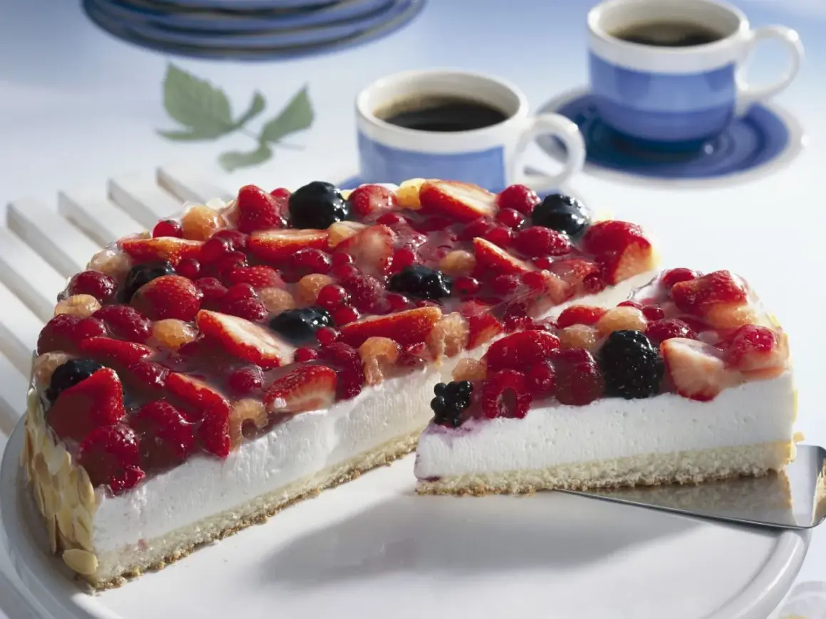 Eine einfache Torte mit frischen Beeren, bedeckt mit Tortenguss. Daneben zwei Tassen Kaffee.