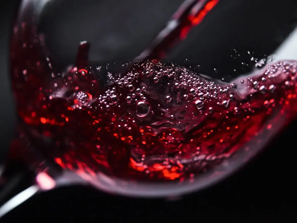 Czerwone wino bez cukru, z bąbelkami unoszącymi się na powierzchni, nalewane do kieliszka.
