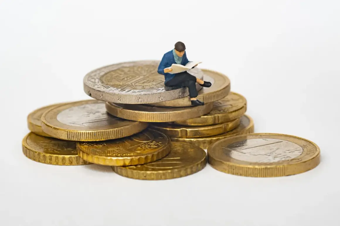Figurka siedząca na stosie monet, czytająca książkę. Symbolizuje mądrość i inwestycje, być może przyszłe wadium.