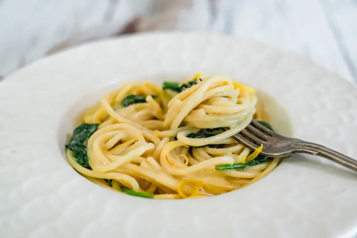 En gaffel lyfter en krämig portion pasta limone med gröna blad och citronskal.