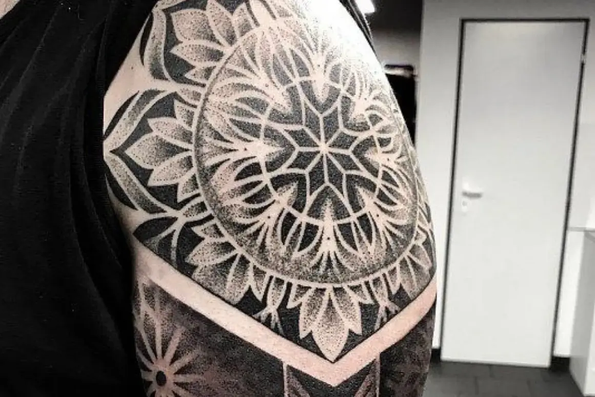 Imponujący tatuaż mandala na ramieniu, wykonany techniką dotwork. Wzór przypomina geometryczny kwiat, otoczony płatkami.