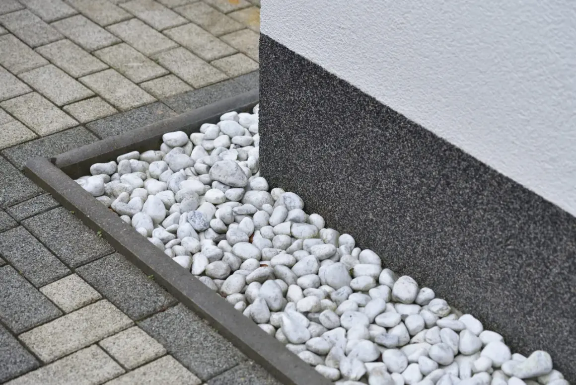 Grus runt huset med stenläggning och en mörk, strukturerad vägg.
