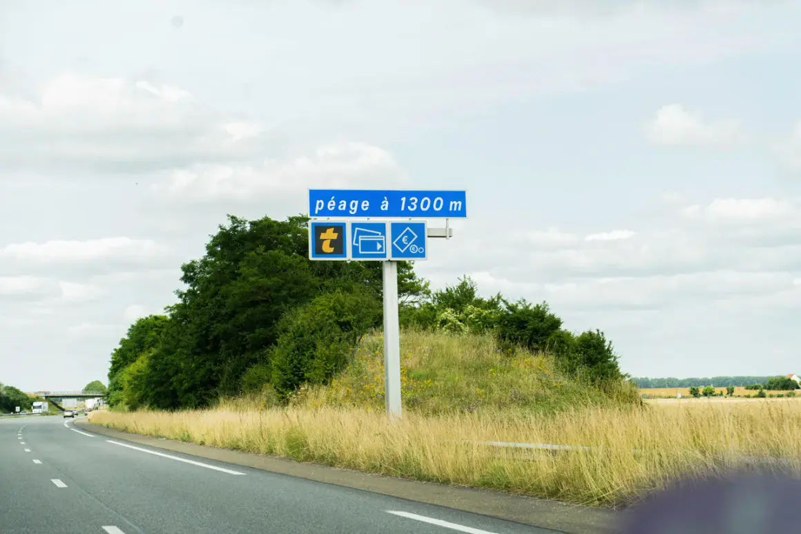 Panneau routier annonçant un péage à 1300m, avec symboles pour télépéage, cartes bancaires et espèces. La route Paris-Nantes se déroule sous un ciel nuageux.
