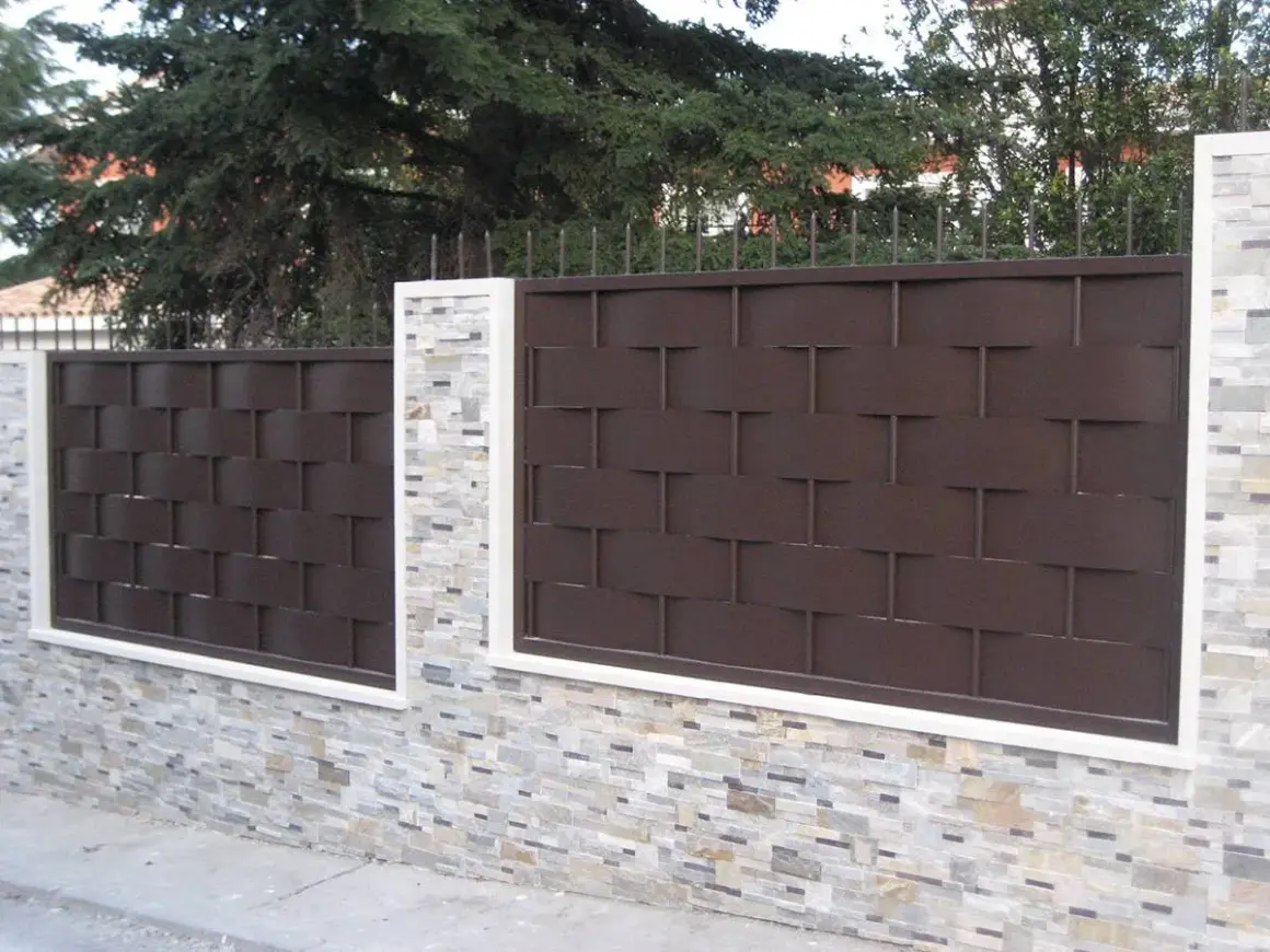 Muro de piedra con paneles de valla de metal marrón oscuro, un ejemplo de tipos de vallas para chalet.