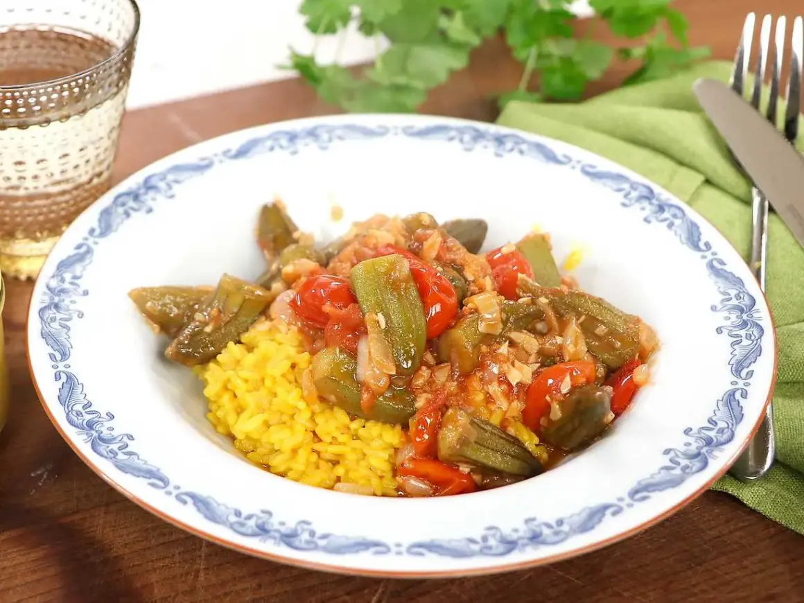 En tallrik med okra och tomater i en kryddig sås, serverad med gul ris. Ett läckert bamya recept för en smakrik måltid.