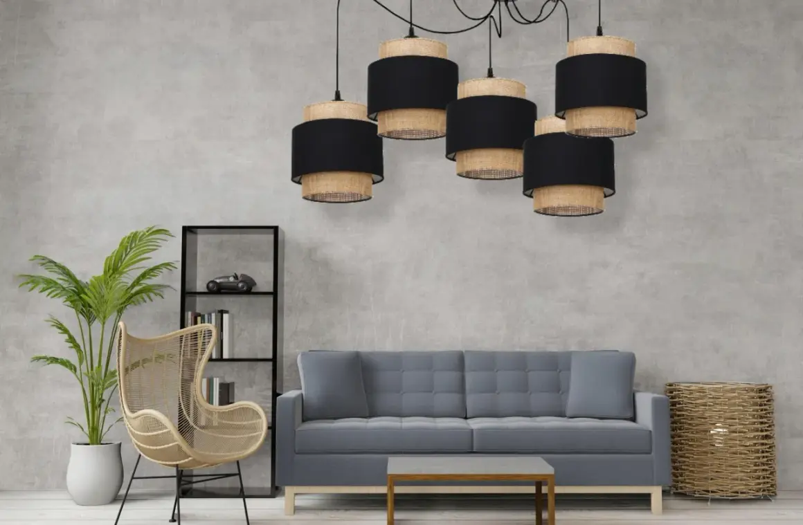 Pięcioramienna lampa pająk boho z abażurami z plecionki i czarnego materiału nad szarą sofą.