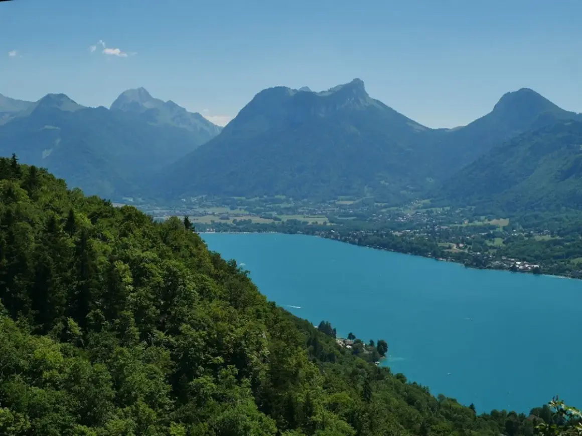 Vue panoramique du lac d'Annecy, ses eaux turquoise bordées de montagnes verdoyantes. Idéal pour un tour du lac Annecy en km.