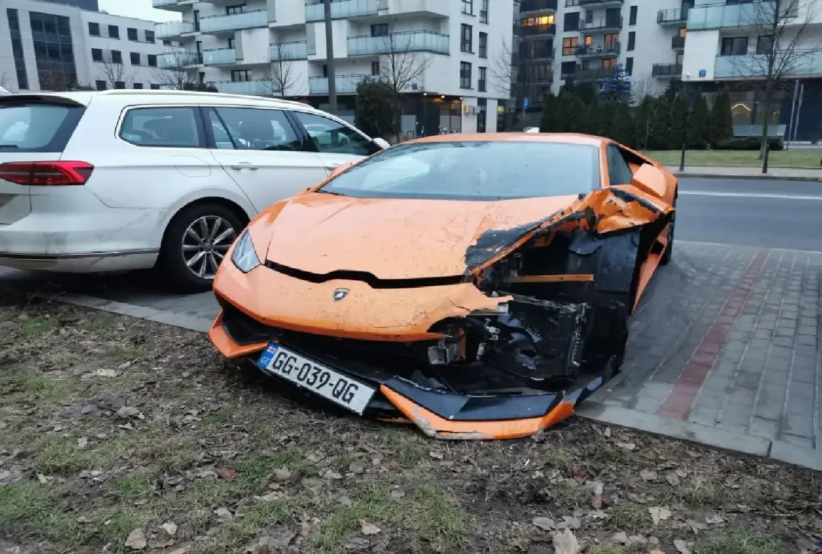 Pomarańczowe lambo po wypadku, przód mocno zniszczony. Obok białe kombi.