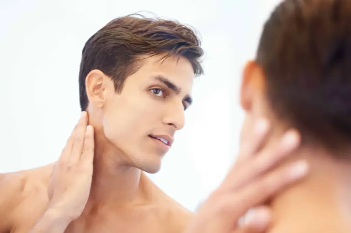 Un homme au visage fin et à la mâchoire marquée, la main caressant son cou, révélant une belle v line.