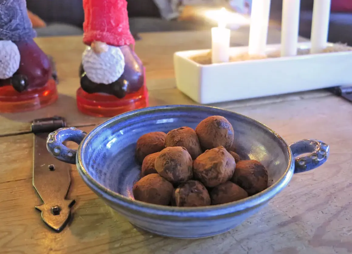 En blå skål med chokladpraliner, perfekta som julgodis utan socker. I bakgrunden syns tomteljus och adventsljusstake.