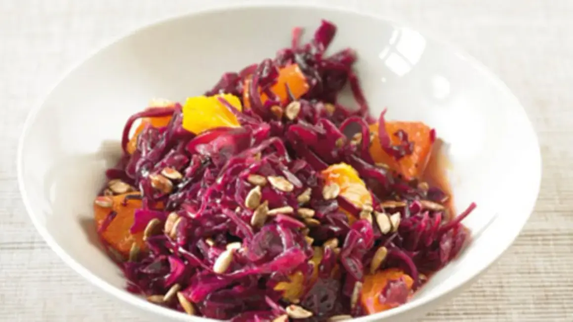 Rotkohlsalat mit Apfel und Orange, garniert mit Sonnenblumenkernen, in einer weißen Schüssel.
